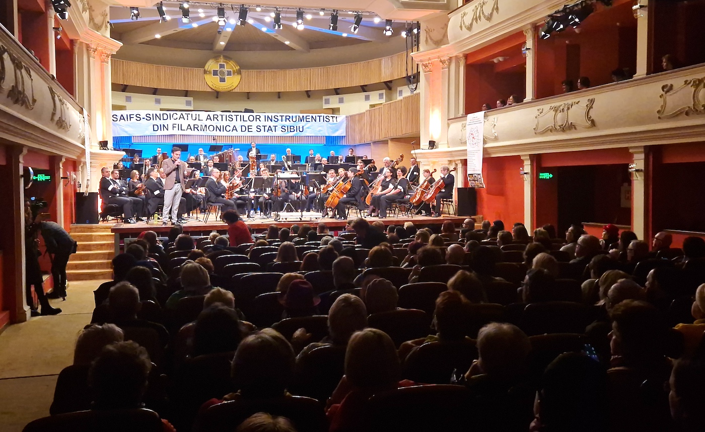Proiect: Filarmonica Sibiu dă afară nouă instrumentiști, inclusiv liderul de sindicat, pe motiv că e mai ieftin să ia colaboratori. Alte nouă posturi se înființează. „Filarmonica încetează să existe ca ansamblu”