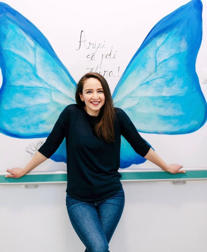 „Prima dată m-au atras artele vizuale, apoi, am descoperit ce înseamnă să lucrezi cu lucruri vechi”. Foto: Nicoleta Opriș și una dintre picturile ei de la pediatria din Făgăraș