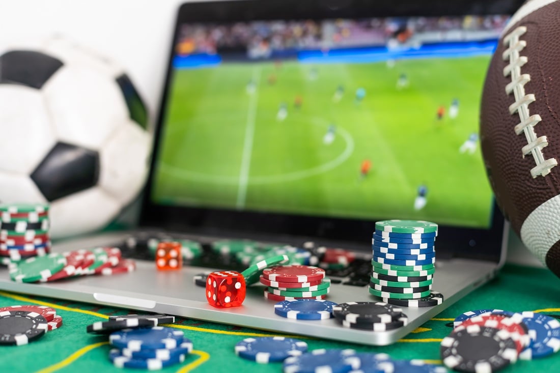 Close up cropped shot of male hands making bets using gambling mobile application on his phone. Man watching football match online broadcast on his laptop waiting for winning results. High quality photo
