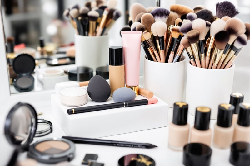 showcases an array of makeup brushes in white holders meticulously arranged alongside various cosmetic products such as foundation powder and sponges. the neutral palette and soft lighting create a clean and sophisticated aesthetic suggesting a professional makeup artist's workspace or a high-end beauty product display.
